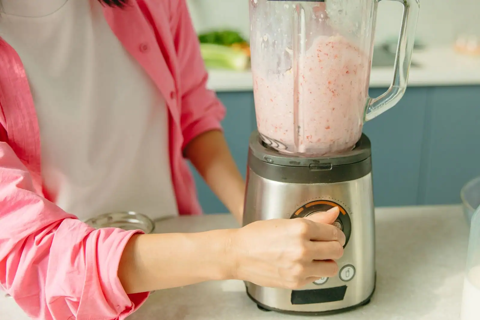 Blender de cuisine en inox dont le bol est rempli d'un smoothie, une main réglant la molette de commande.
