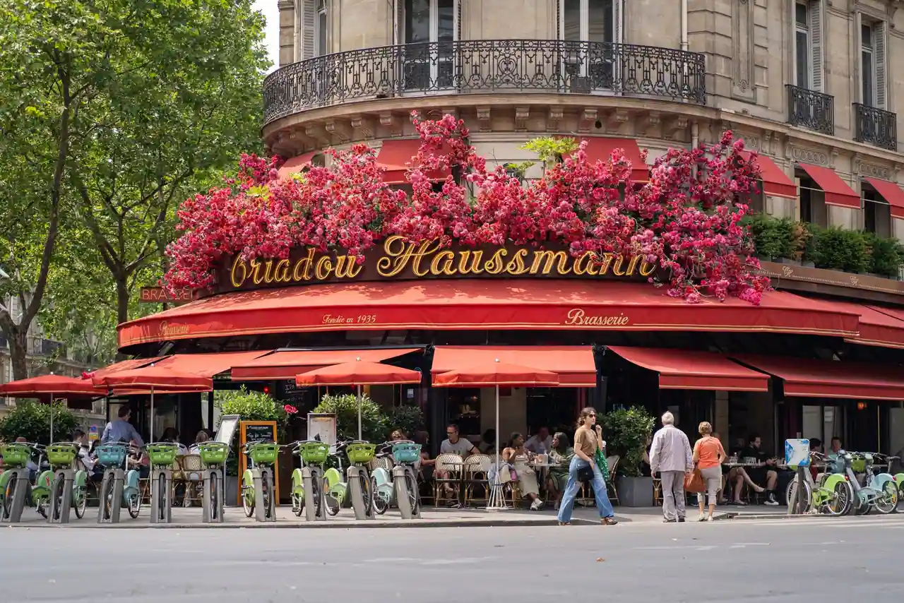 Terrasse animée et devanture fleurie d'un grand café-brasserie parisien, près de l'Opéra.