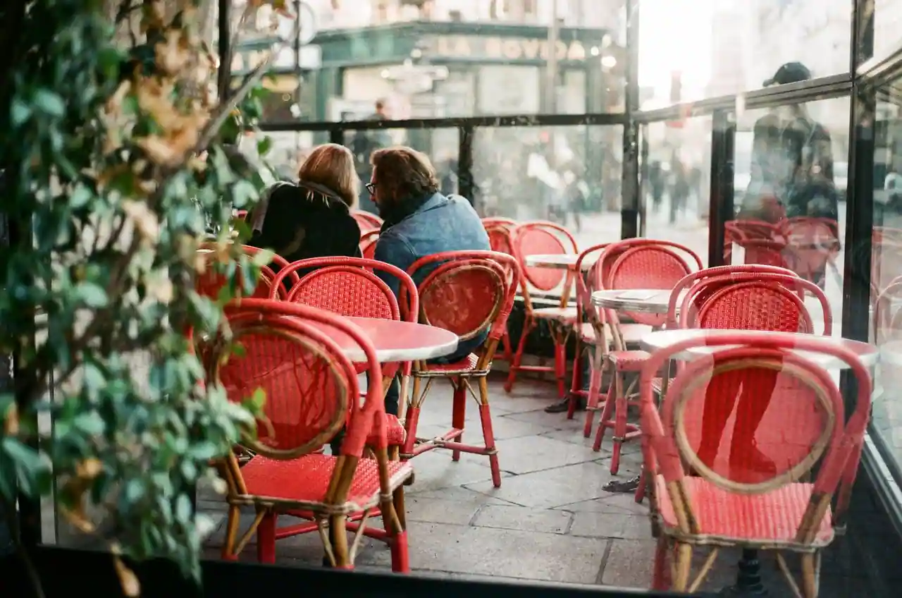 Terrasse d'un café parisien aux chaises rouges en rotin, deux clients attablés