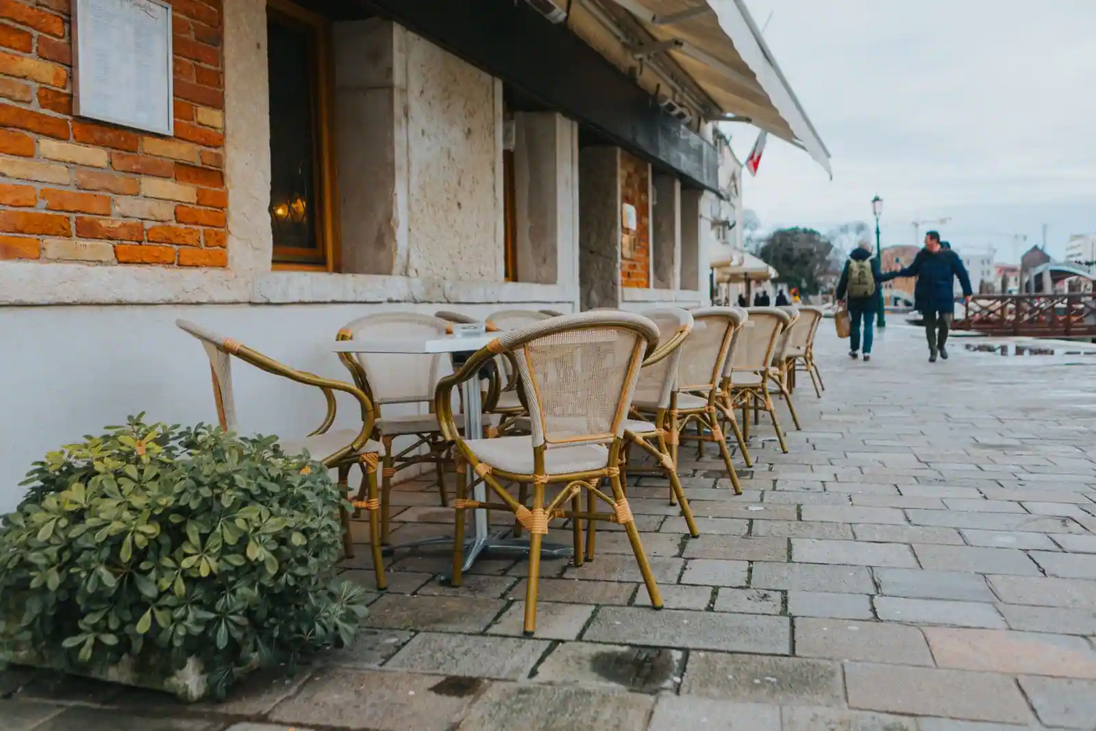Rangée de chaises en rotin et de tables le long de la devanture d'un café, sur une rue pavée.