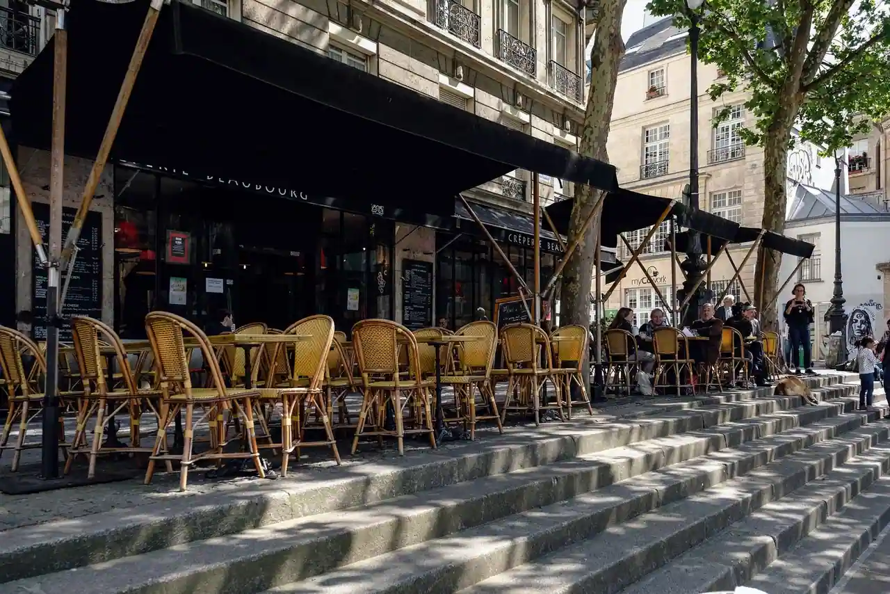 Terrasse de café parisienne aux chaises en rotin et petites tables sur le trottoir, au soleil.