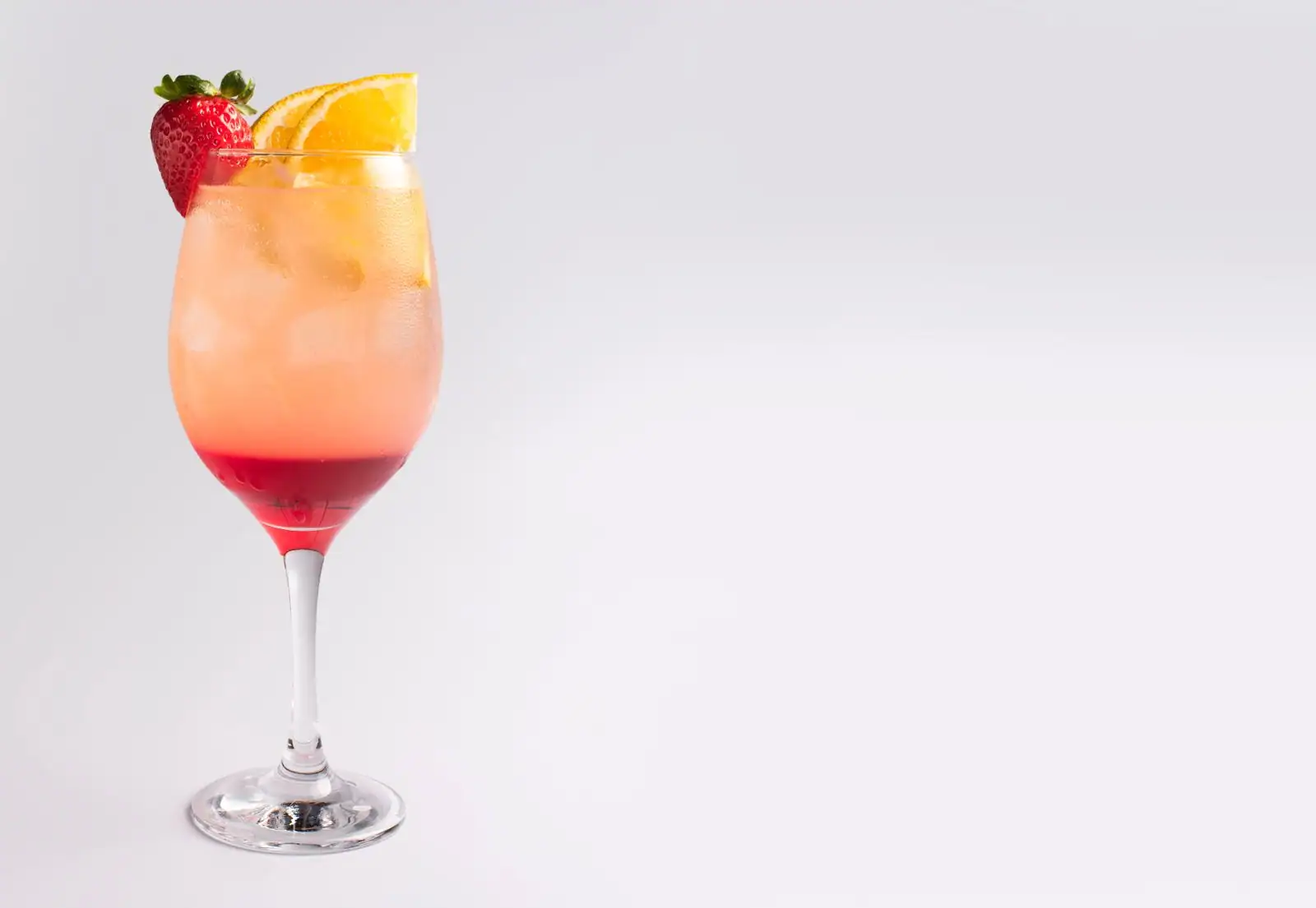 Cocktail au dégradé orange et rouge dans un verre à pied, garni d'une fraise et d'une tranche d'orange.