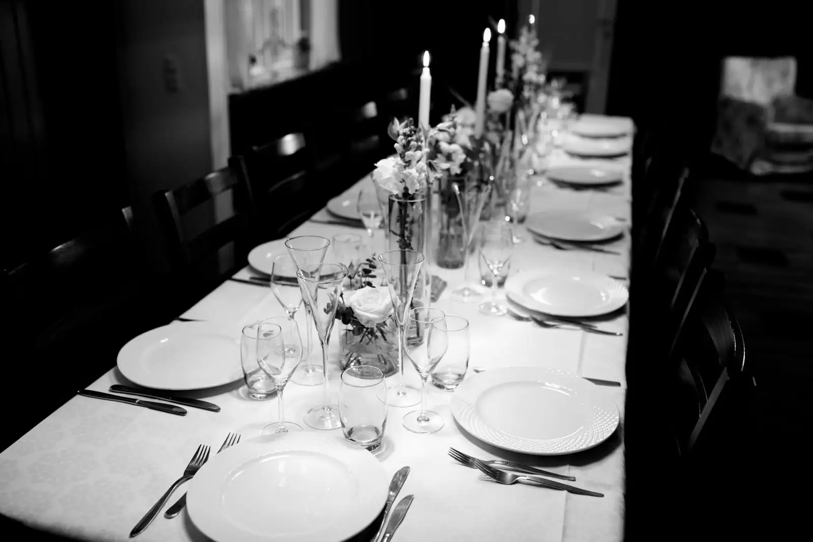Table de fête dressée avec assiettes, couverts, verres, bougies et fleurs en centre de table