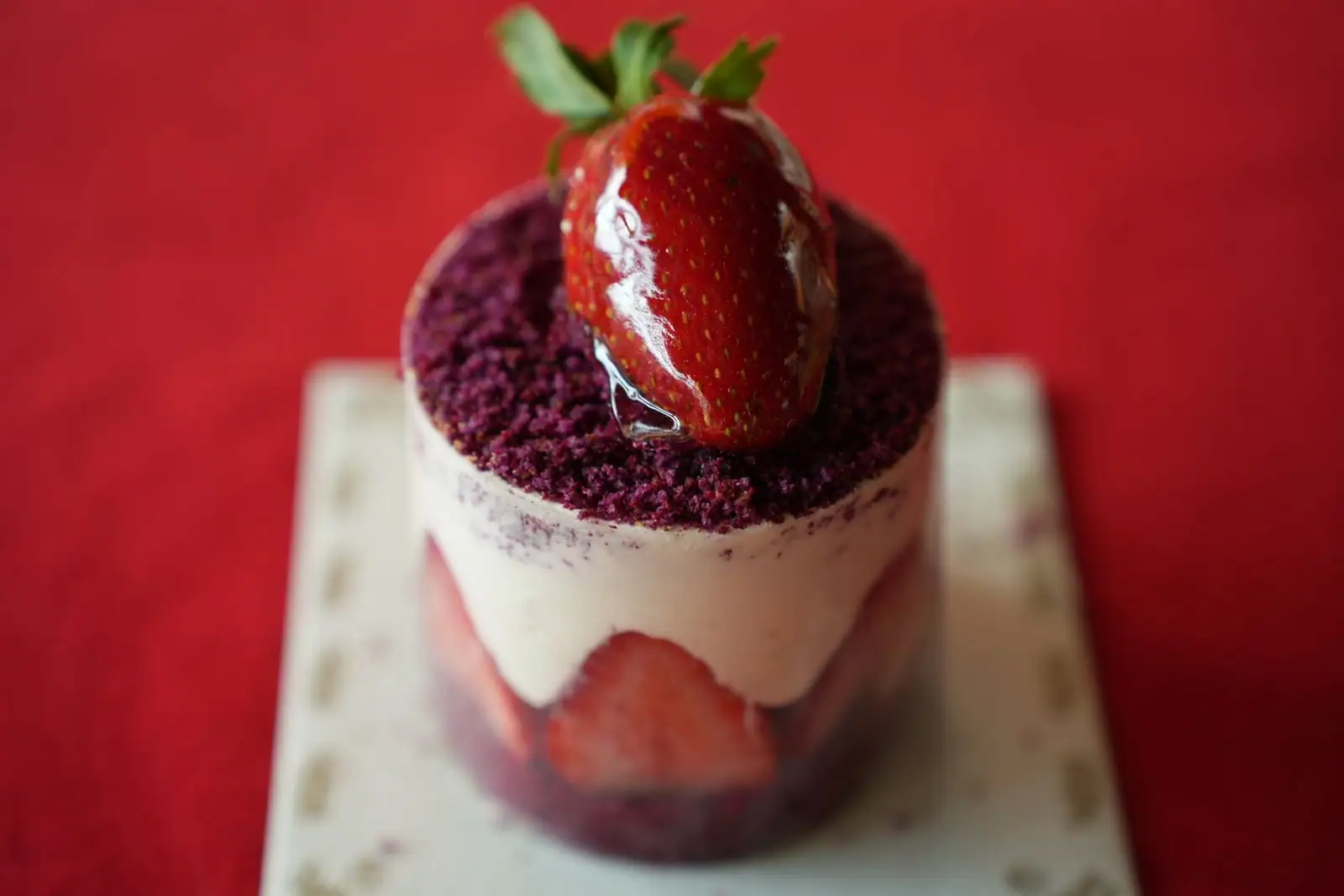 Verrine de dessert à la crème, fraise et crumble, présentée sur une petite assiette.