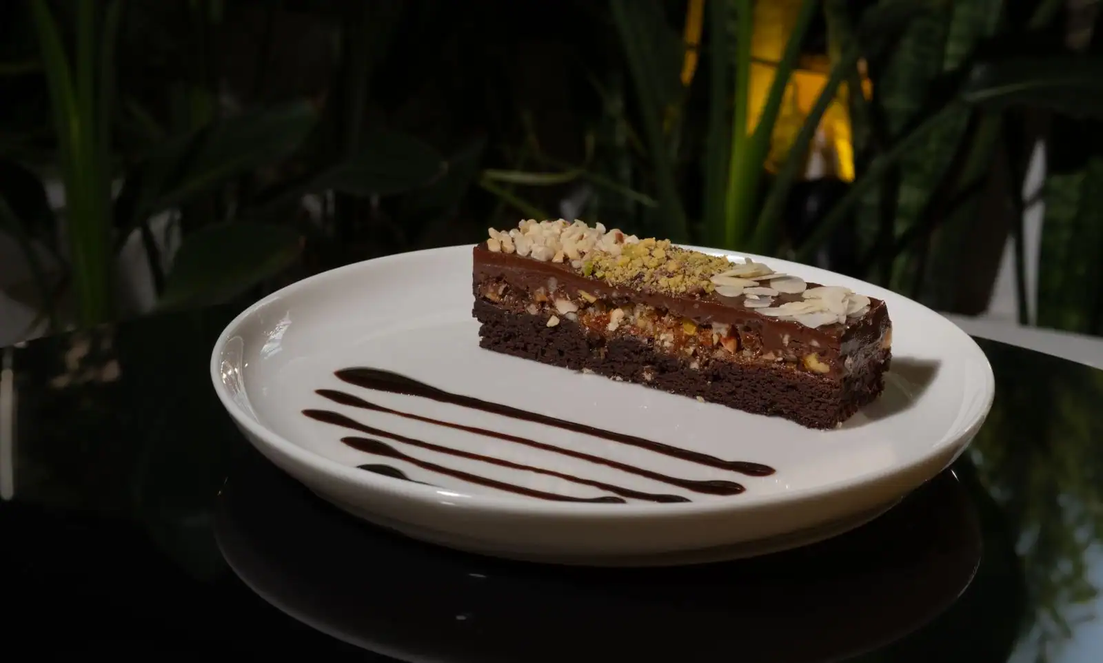 Part de gâteau au chocolat surmontée d'amandes concassées, sur une assiette claire avec un filet de chocolat.