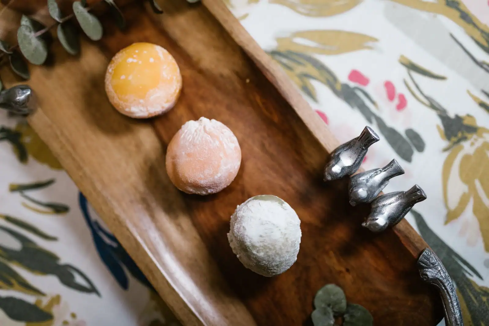 Trois mochis japonais saupoudrés, jaune, rosé et blanc, posés sur une planche en bois.