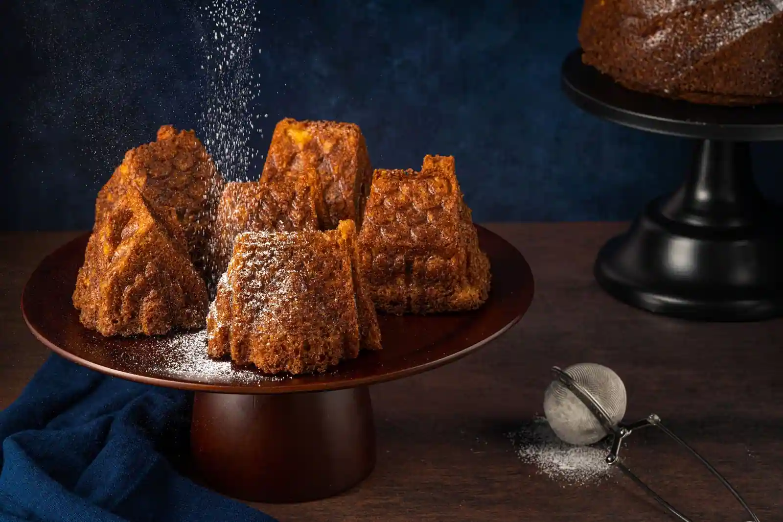 Parts d'un gâteau doré à la texture cannelée, saupoudrées de sucre glace sur un présentoir en bois.