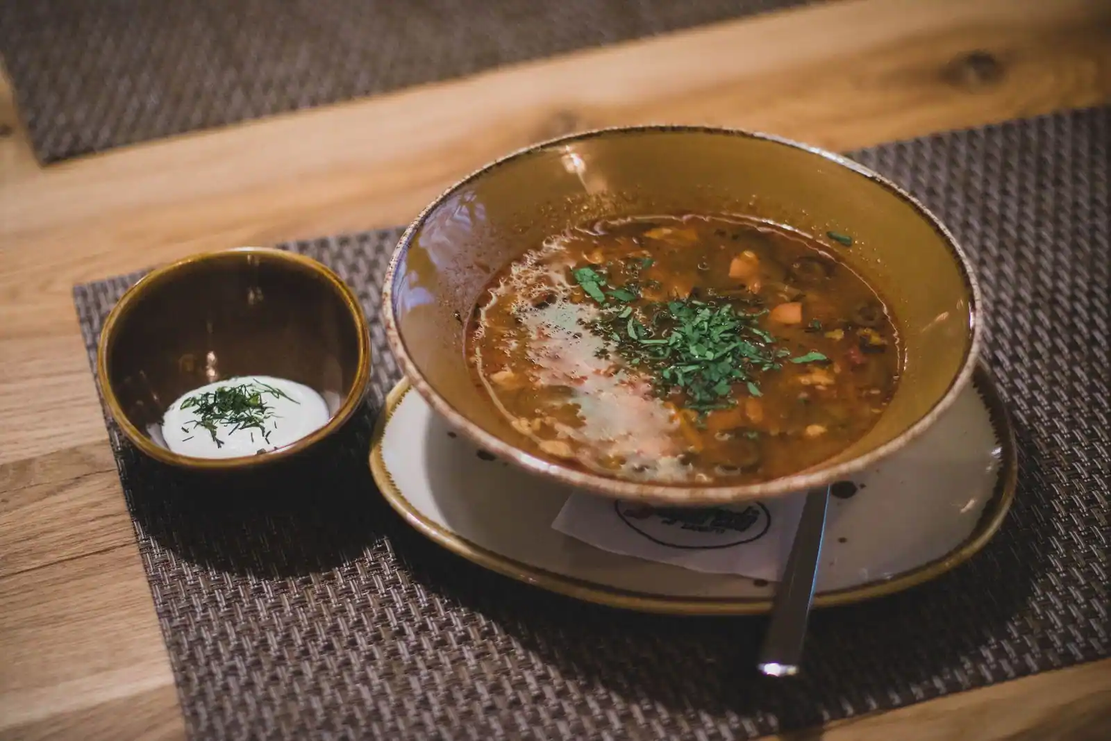 Bol de soupe chaude garnie d'herbes, servie avec une coupelle de crème, en entrée.