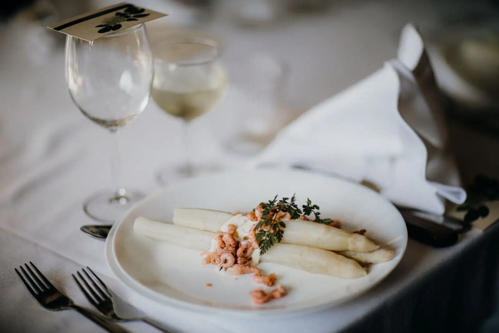 Assiette d'asperges blanches aux crevettes et à la crème, dressée sur une table de fête avec des verres de vin.