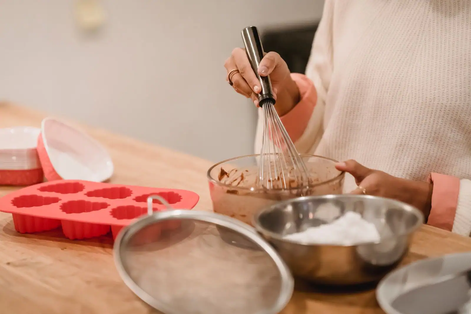 Préparation d'une pâte au fouet, avec moule en silicone et bols sur un plan de travail en bois.