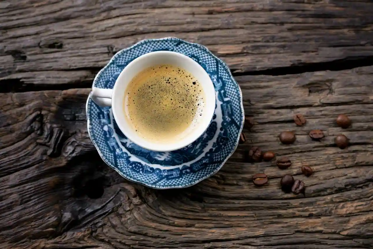 Tasse de café à la crema dorée, posée près de quelques grains de café sur une table en bois.