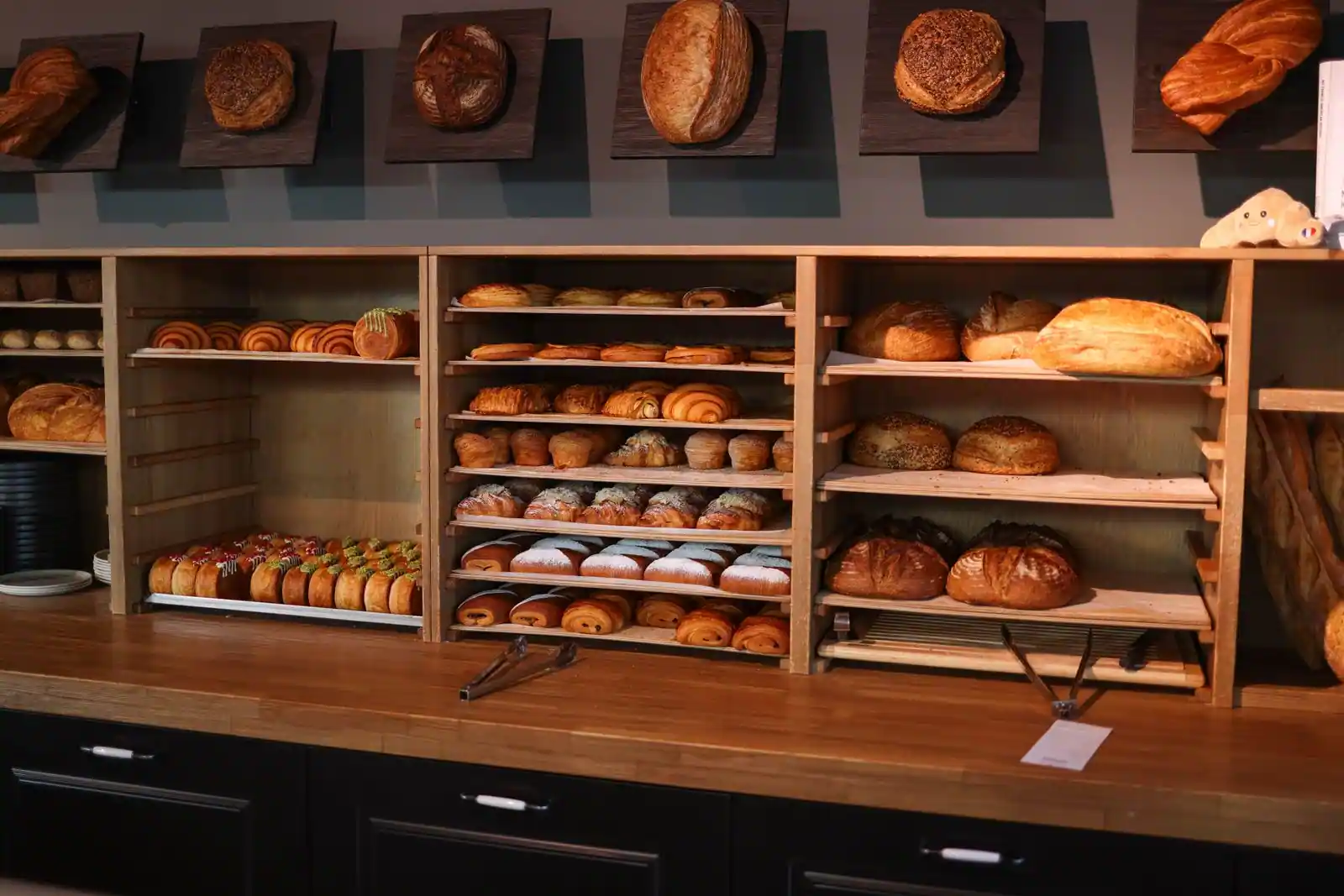 Étagères en bois garnies de pains, miches et viennoiseries dans une boulangerie.