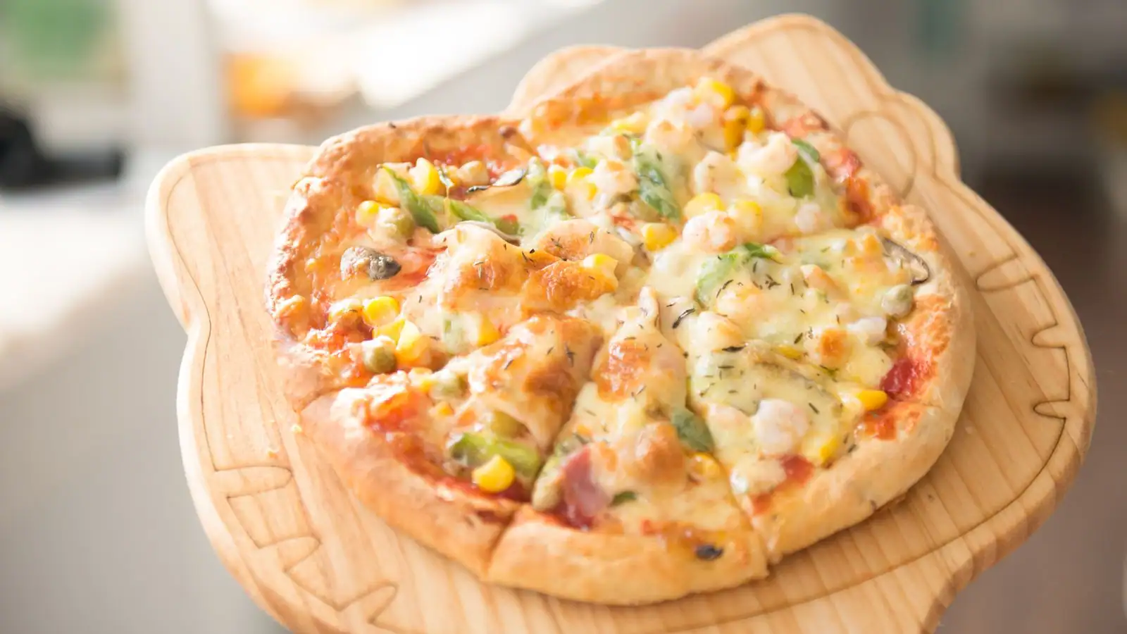 Pizza maison découpée en parts, garnie de fromage, de maïs et de légumes, sur une planche en bois