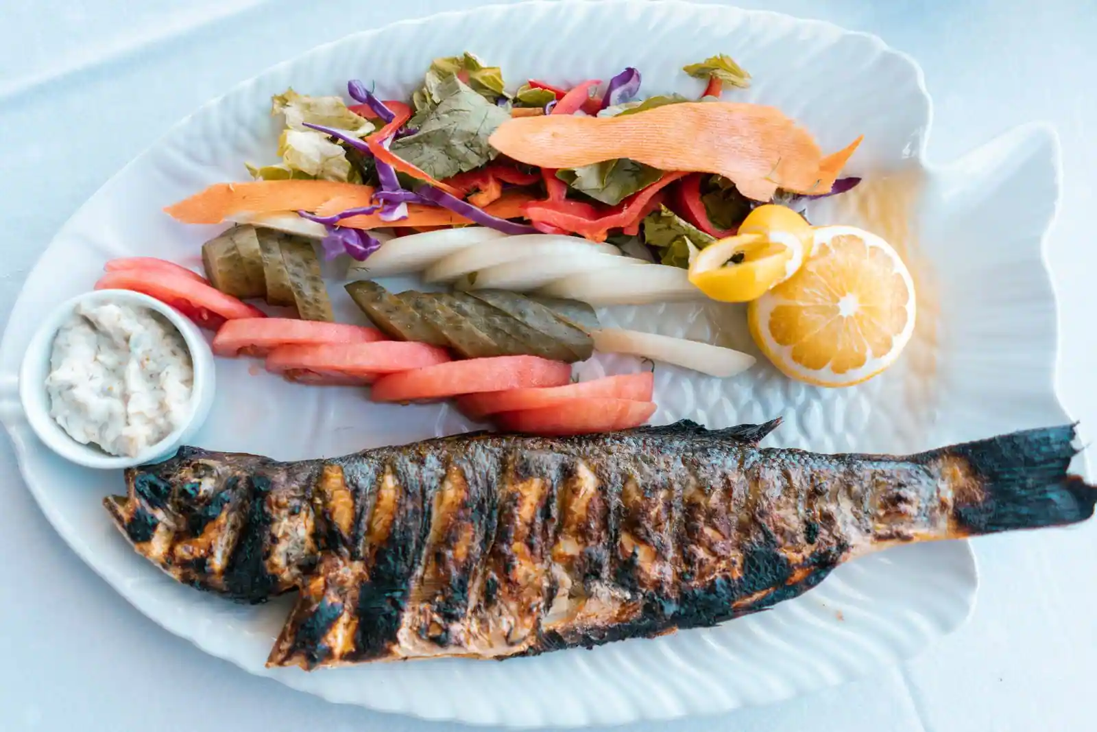 Poisson entier grillé accompagné d'une salade de légumes frais, de citron et d'une sauce