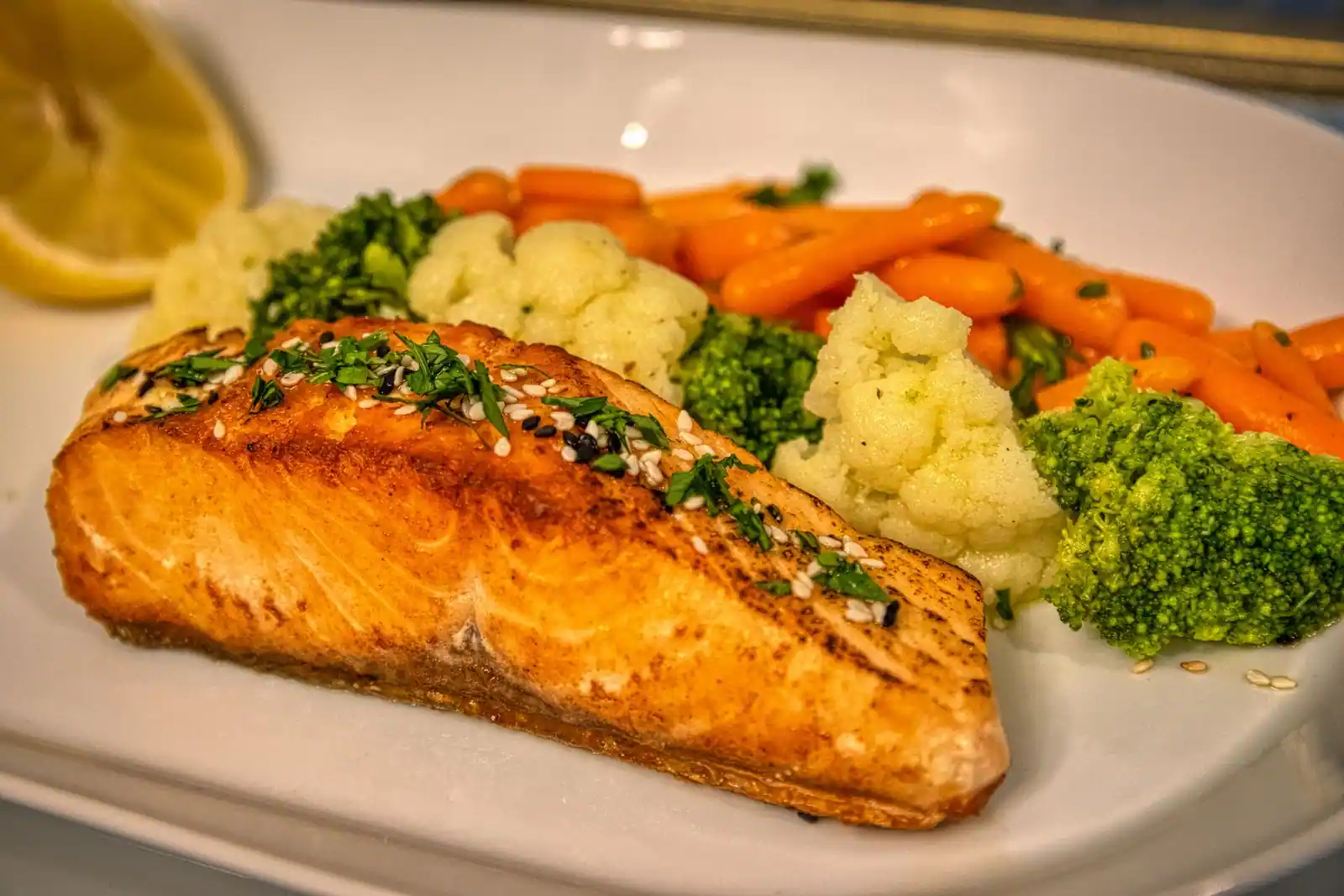 Filet de saumon grillé au sésame accompagné de brocolis, chou-fleur et carottes vapeur dans une assiette.