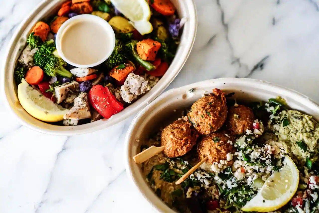 Deux bols de légumes rôtis, viande grillée et salade, posés sur une table en marbre