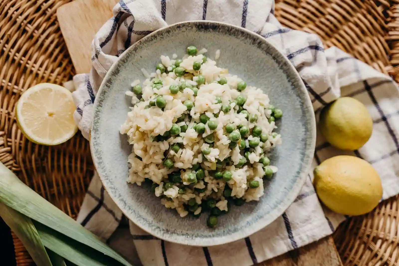 Assiette de risotto crémeux et verdoyant, accompagnée d'un poireau frais et de citrons sur une nappe rustique