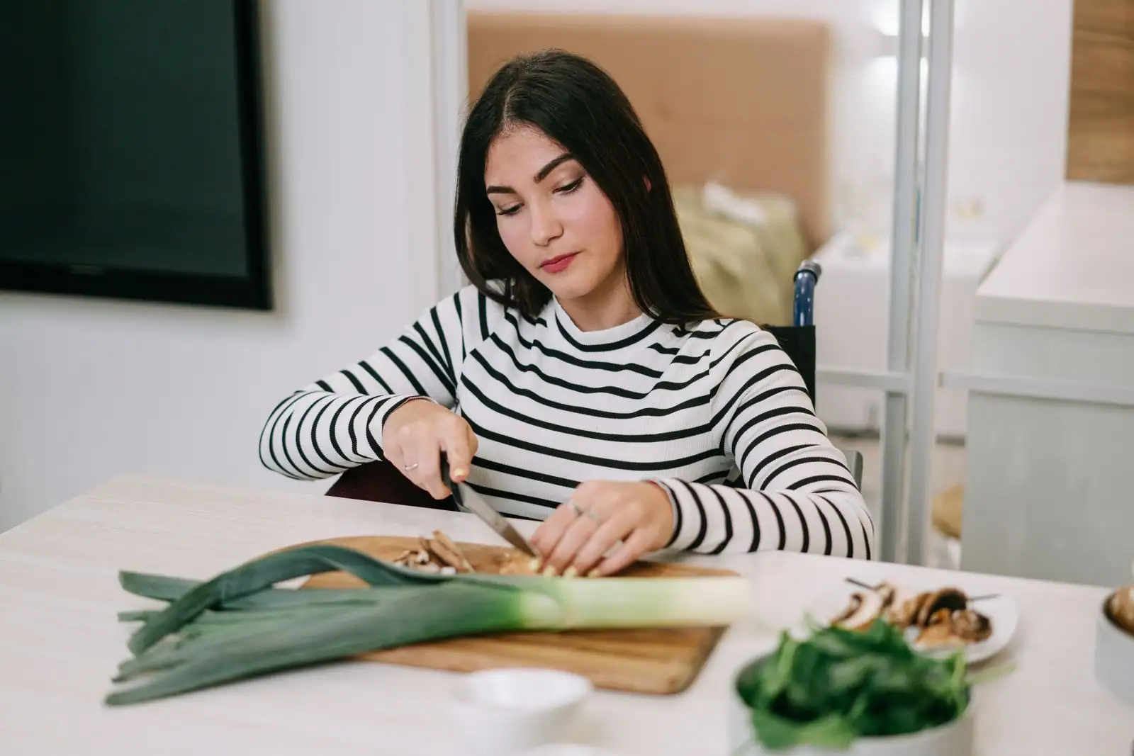 Femme éminçant un poireau sur une planche en bois dans une cuisine, poireaux entiers posés à côté.