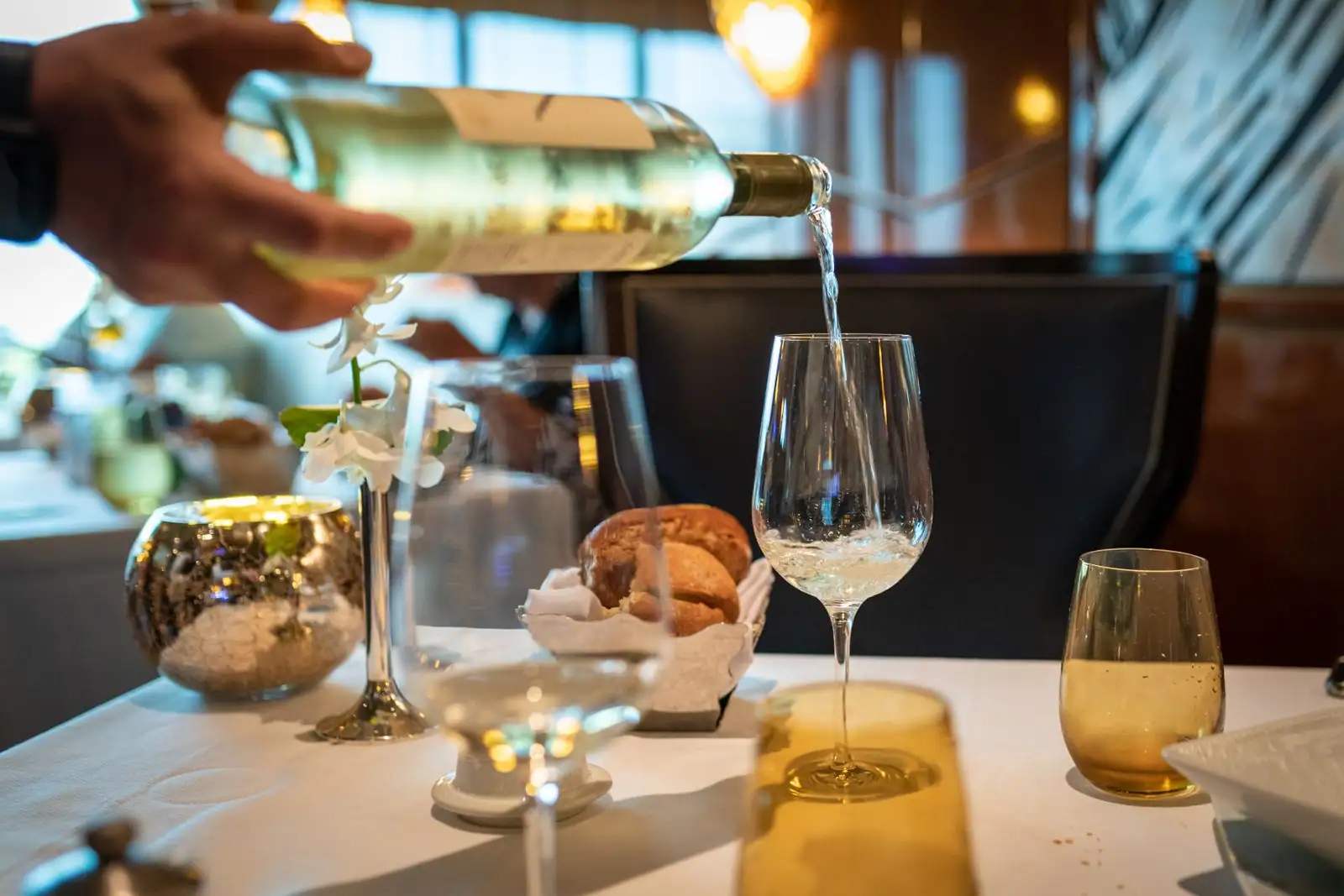 Service d'un vin blanc : une main verse la bouteille dans un verre à pied, sur une table dressée