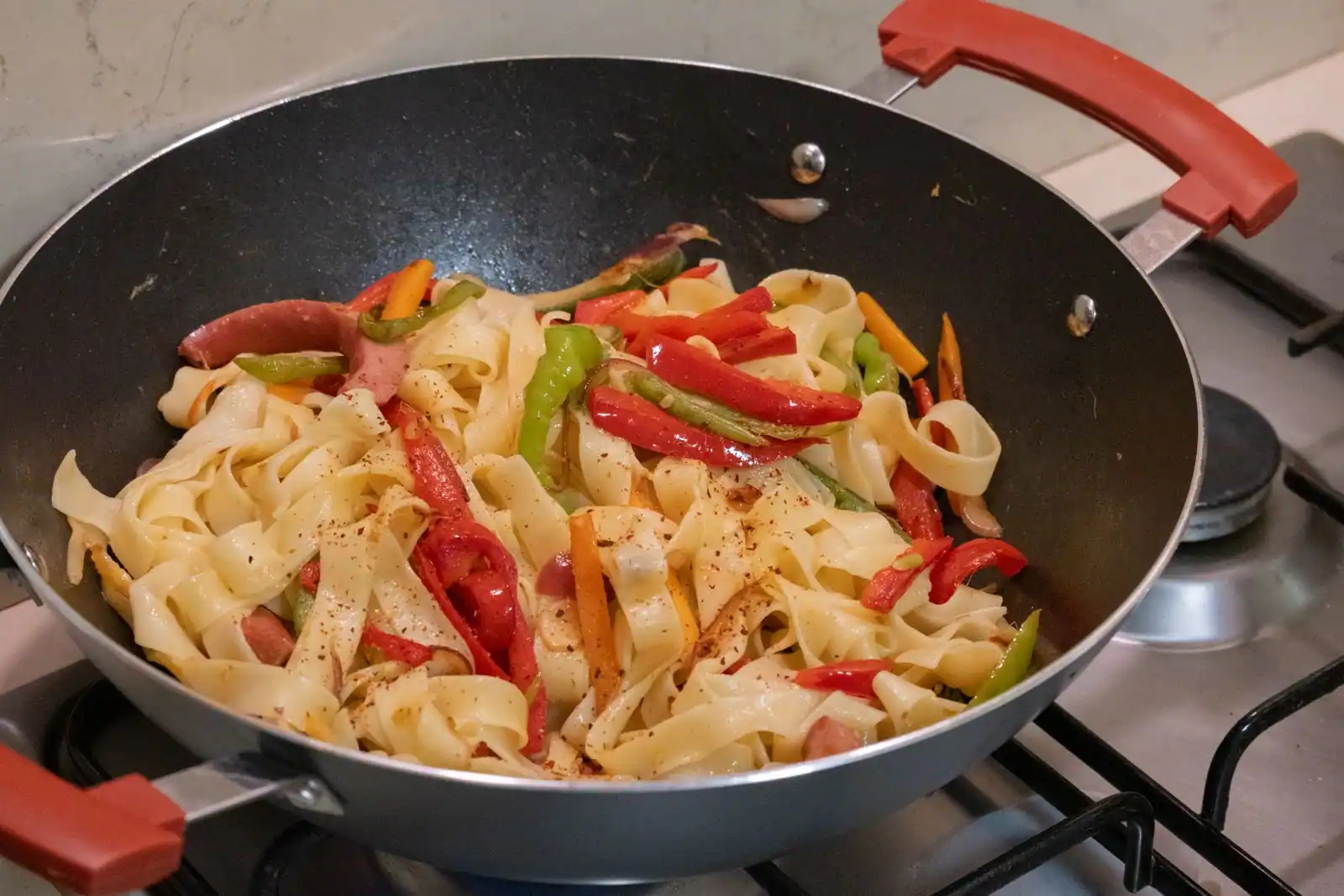 Wok garni de nouilles plates, de poivrons et de carottes posé sur une cuisinière à gaz