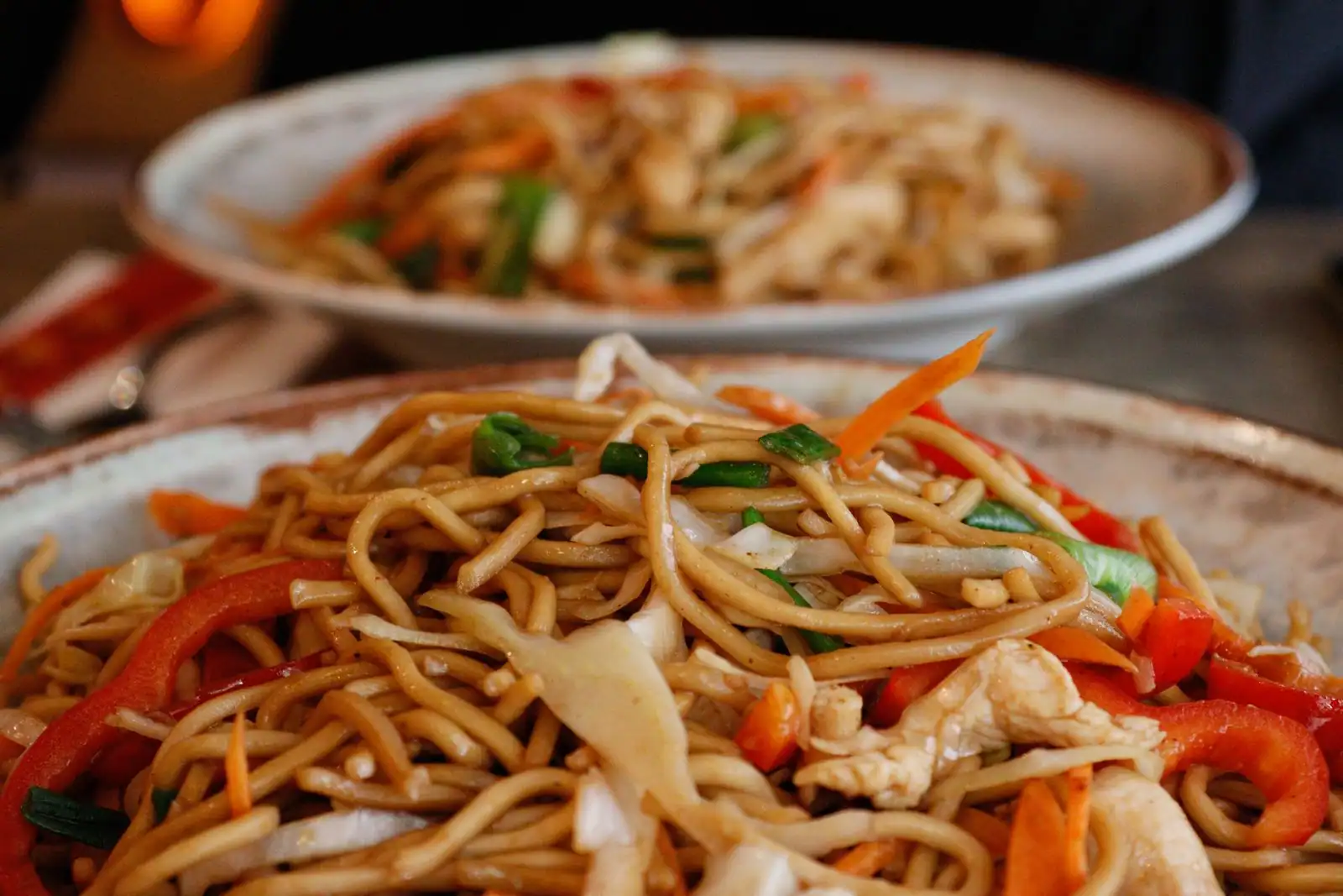 Deux assiettes de nouilles sautées aux légumes, poivron et poulet, façon plat asiatique.