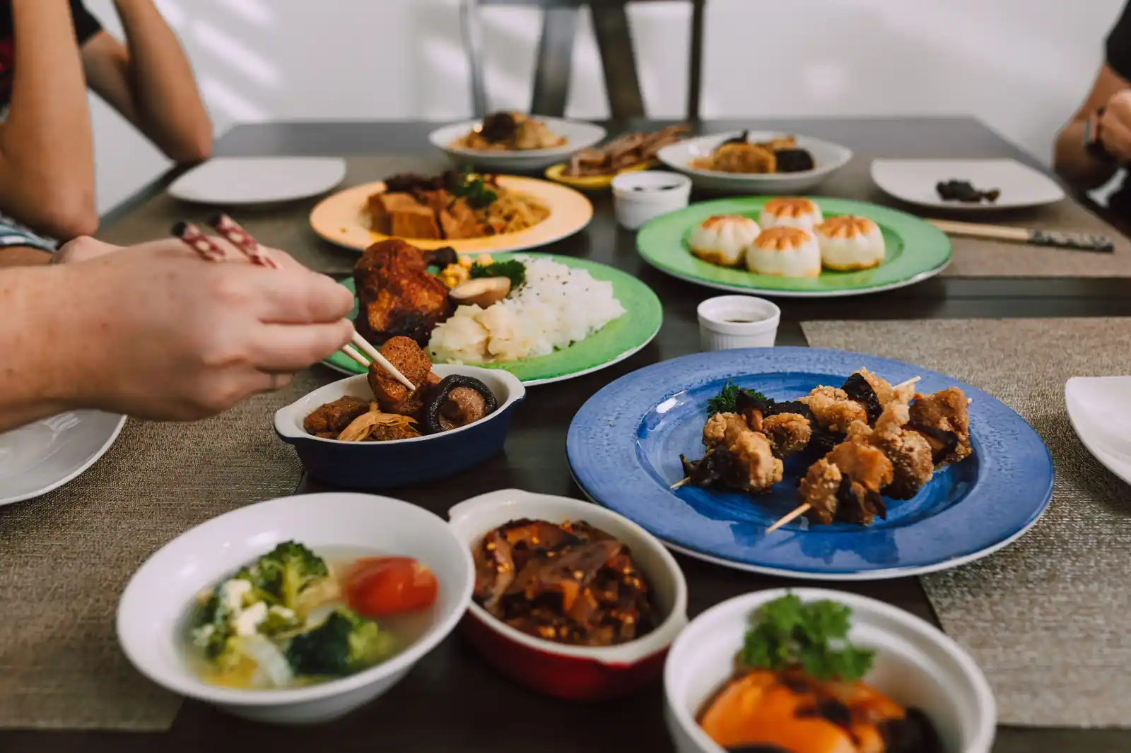 Table garnie de plusieurs plats asiatiques à partager : riz, petits pains fourrés, brochettes panées et soupe