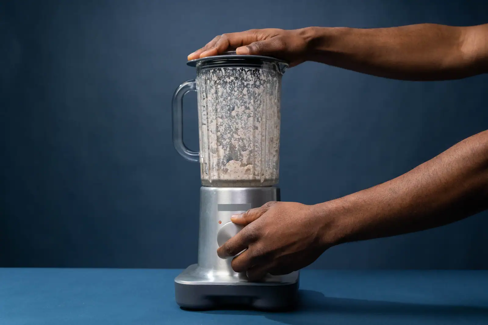 Blender de comptoir tenu à deux mains, bol en verre couvert posé sur son socle moteur métallique