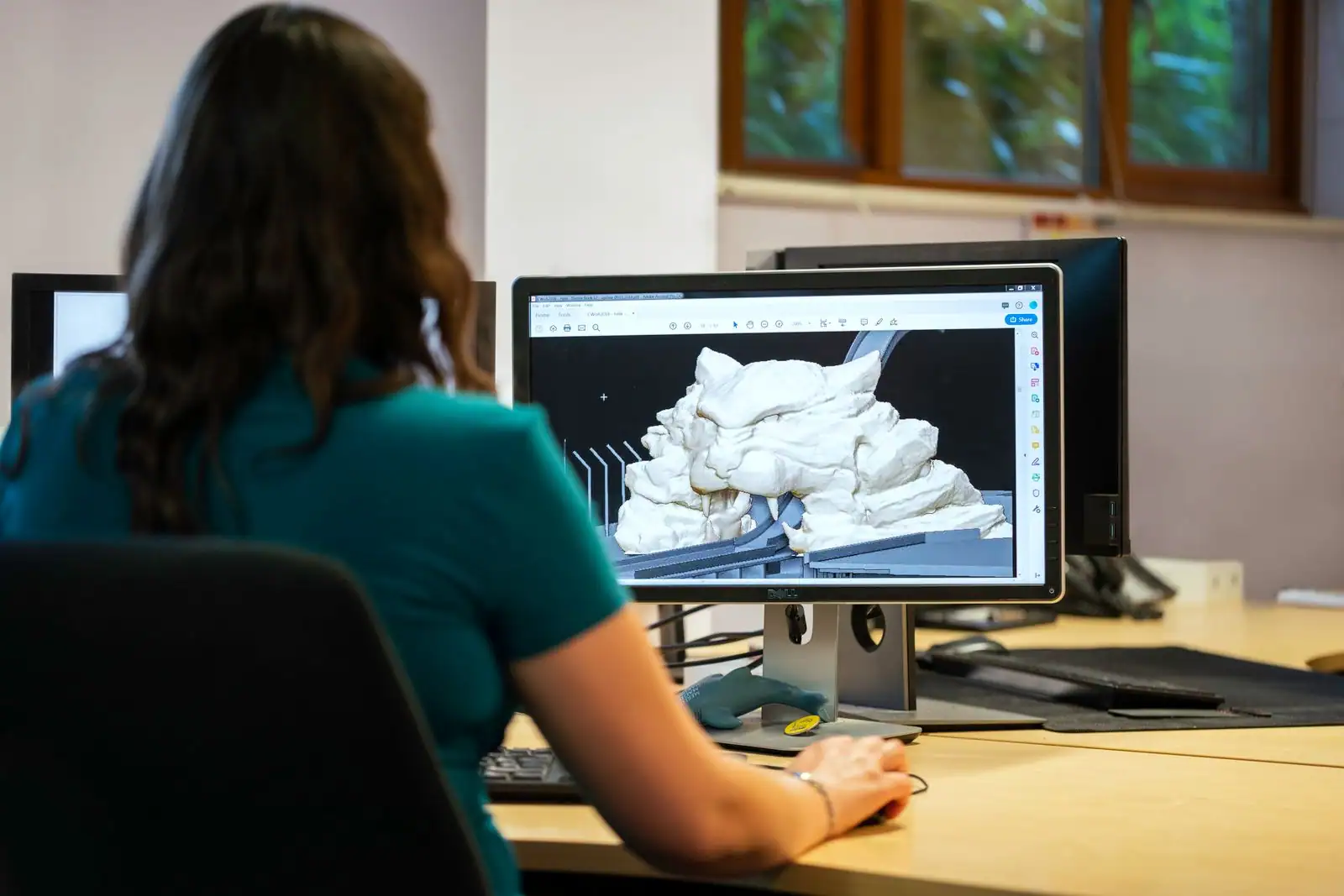 Personne de dos face à un écran affichant un modèle 3D dans un logiciel de modélisation.