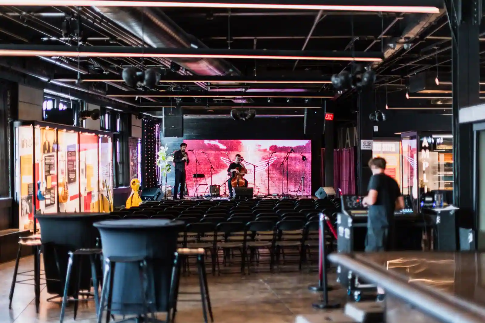 Petite salle de concert intimiste : scène éclairée, musiciens et rangées de chaises face au plateau.