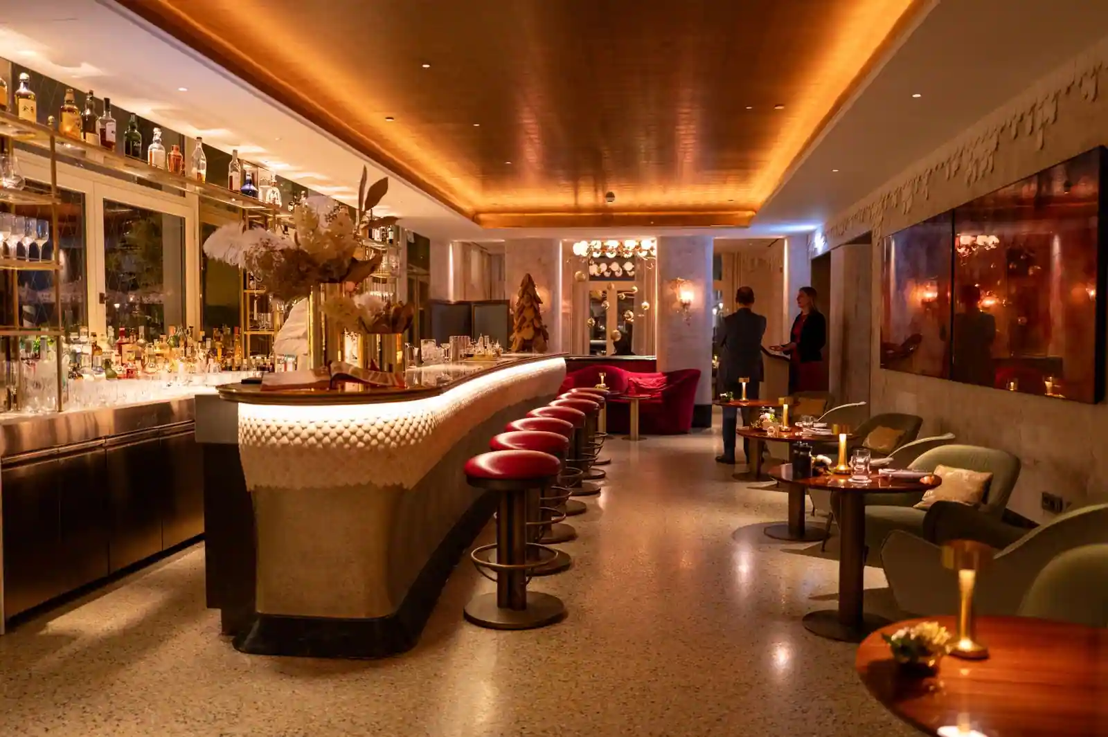 Intérieur chic d'un bar-restaurant parisien avec long comptoir, tabourets de velours rouge et éclairage feutré
