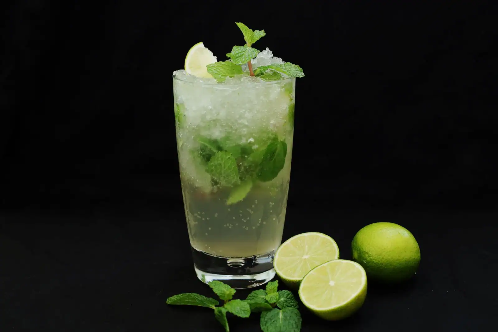 Verre de cocktail garni de menthe fraîche, citron vert et glace pilée, posé sur un fond sombre