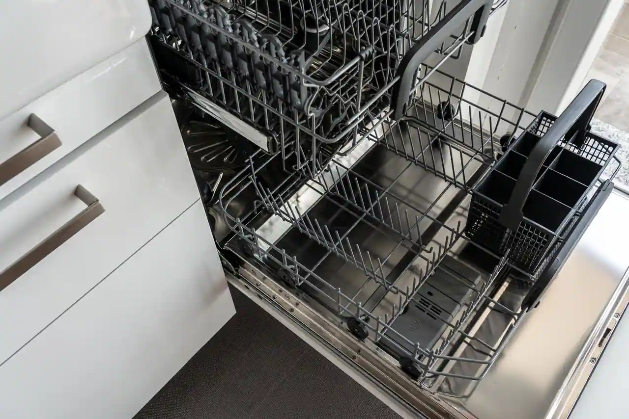 Intérieur d'un lave-vaisselle ouvert montrant les deux paniers vides et le panier à couverts, dans une cuisine