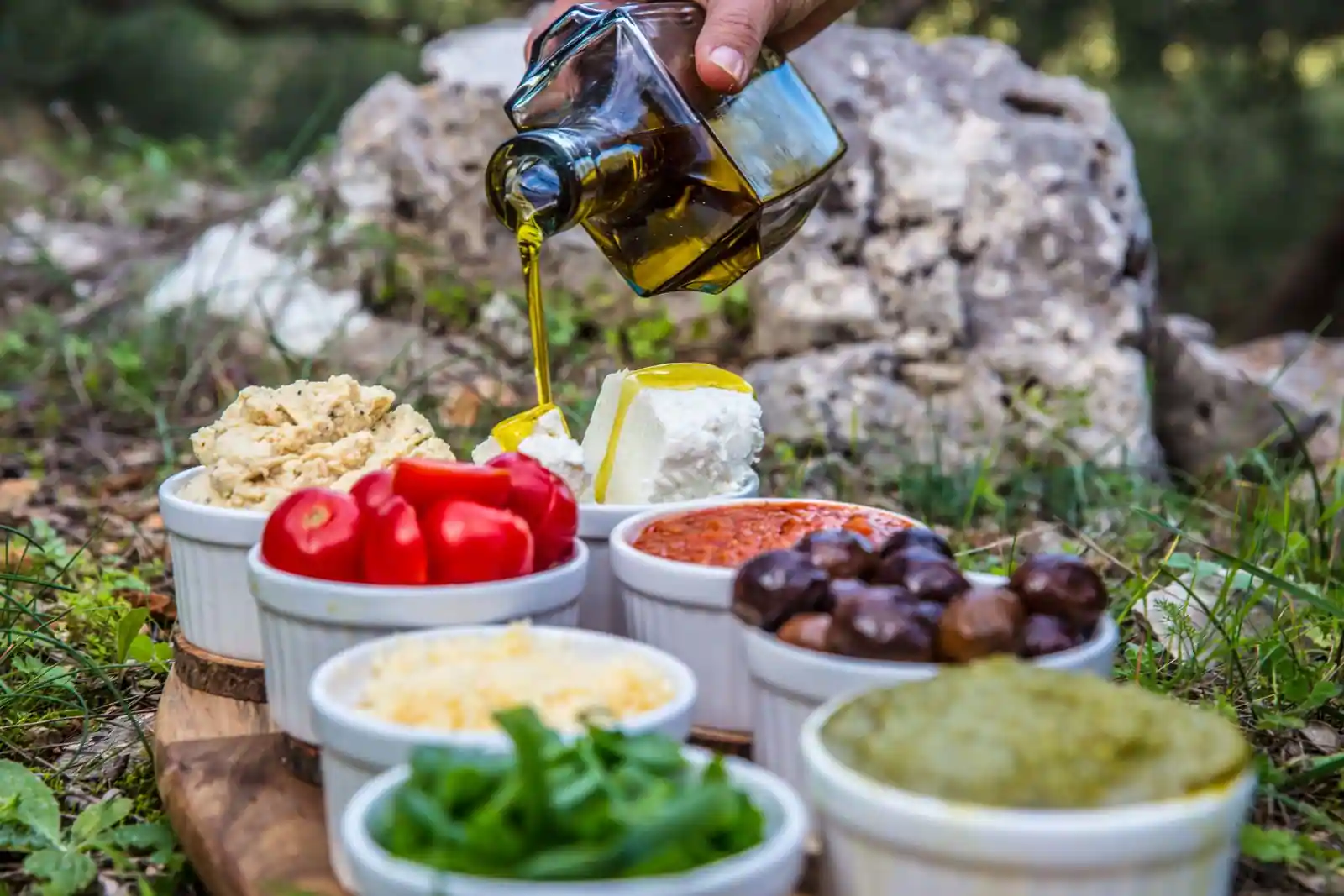 Petits plats méditerranéens en coupelles — houmous, tomates, feta, olives — et huile d'olive versée.