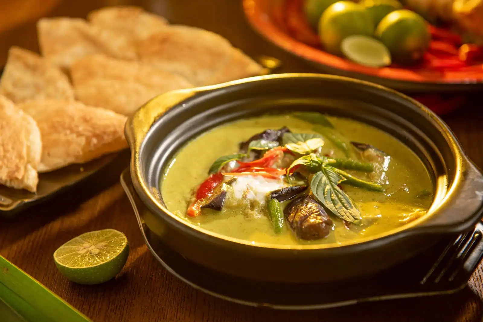 Curry vert thaïlandais dans un bol en terre, garni de basilic thaï et de piment, avec citron vert et pain