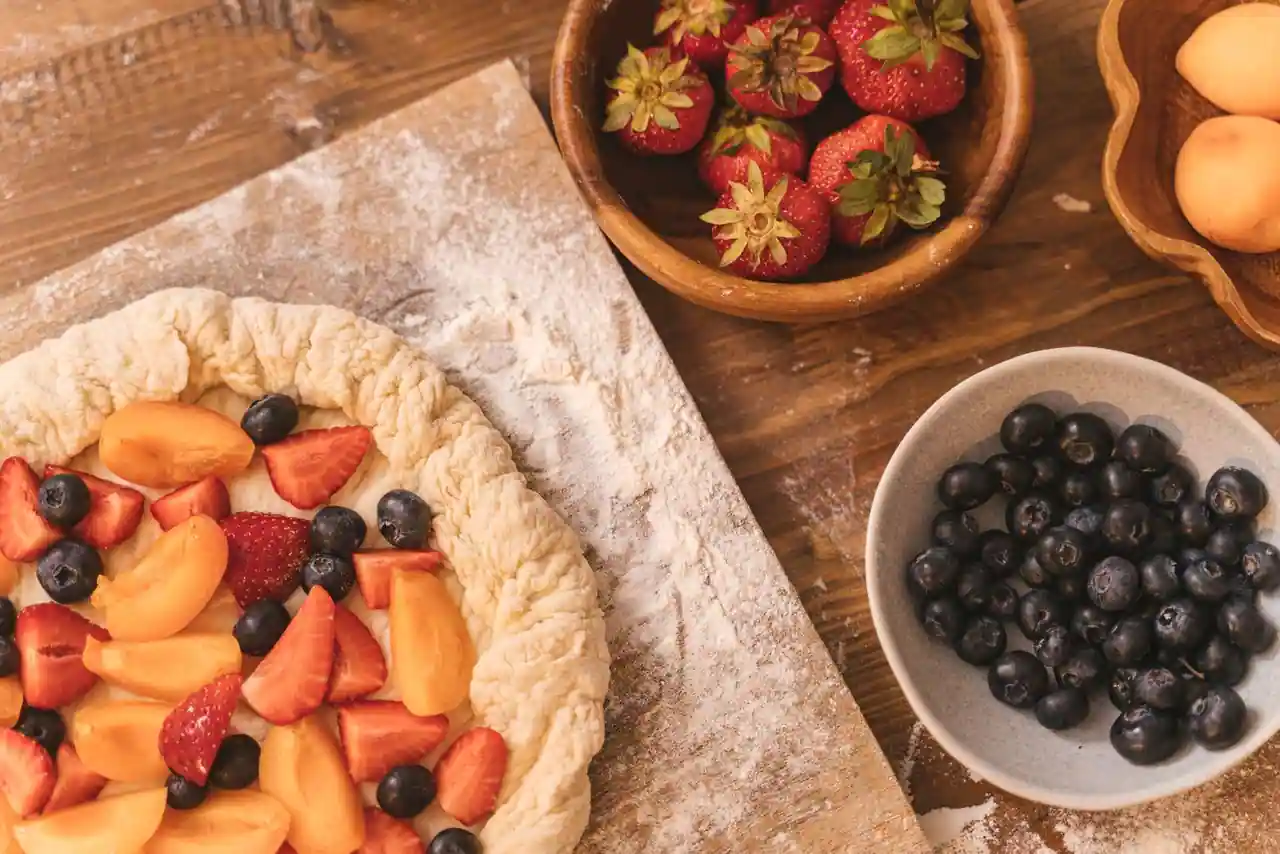 Tarte rustique aux fruits en préparation, garnie d'abricots et de fruits rouges, sur un plan fariné.