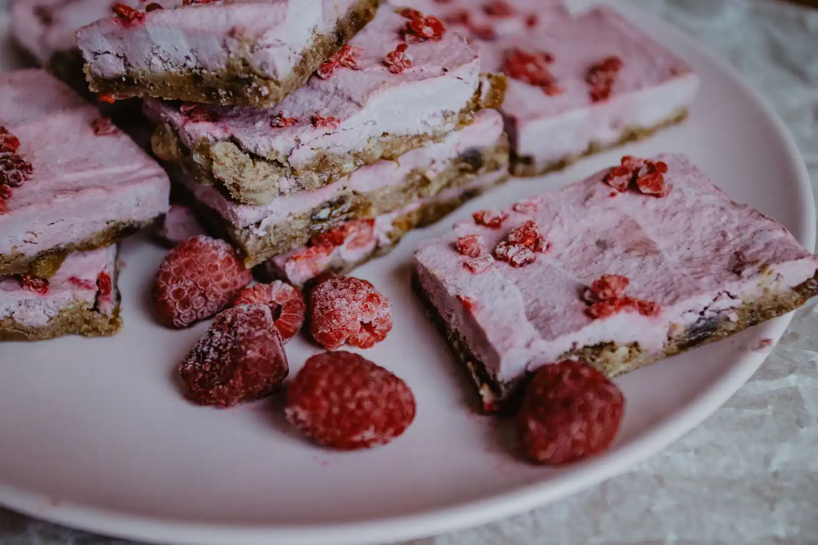 Parts de dessert glacé rosé sur base biscuitée, servies avec des framboises surgelées
