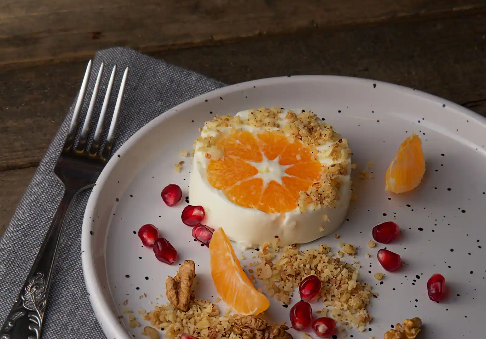 Petit dessert à la crème surmonté d'une tranche de mandarine, avec éclats de noix et grains de grenade