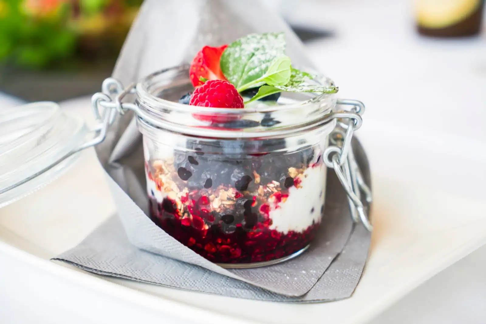 Verrine de fromage blanc, muesli et compote de fruits rouges garnie d'une framboise et de menthe fraîche