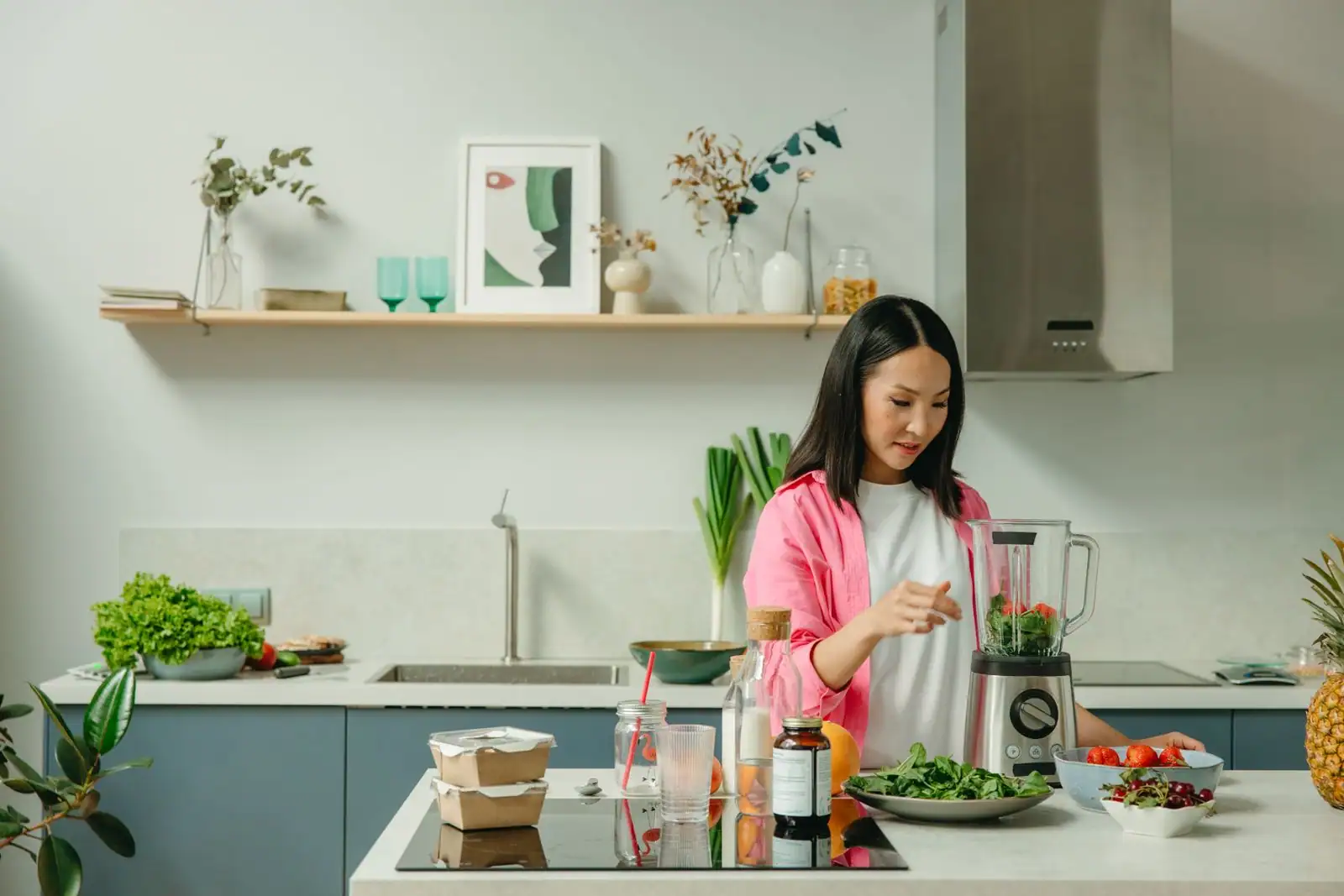 Personne préparant des légumes verts dans un blender posé sur un îlot de cuisine