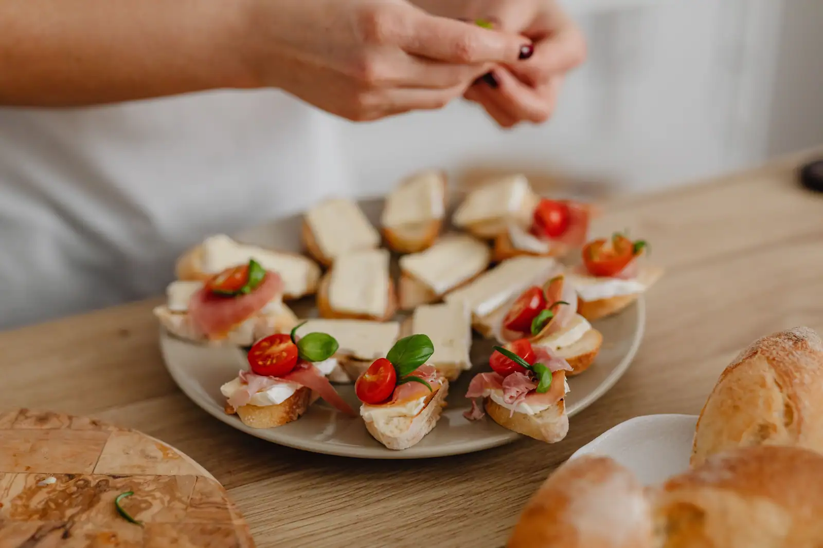 Assemblage de petits toasts au fromage frais, jambon cru, tomate cerise et basilic sur une assiette.