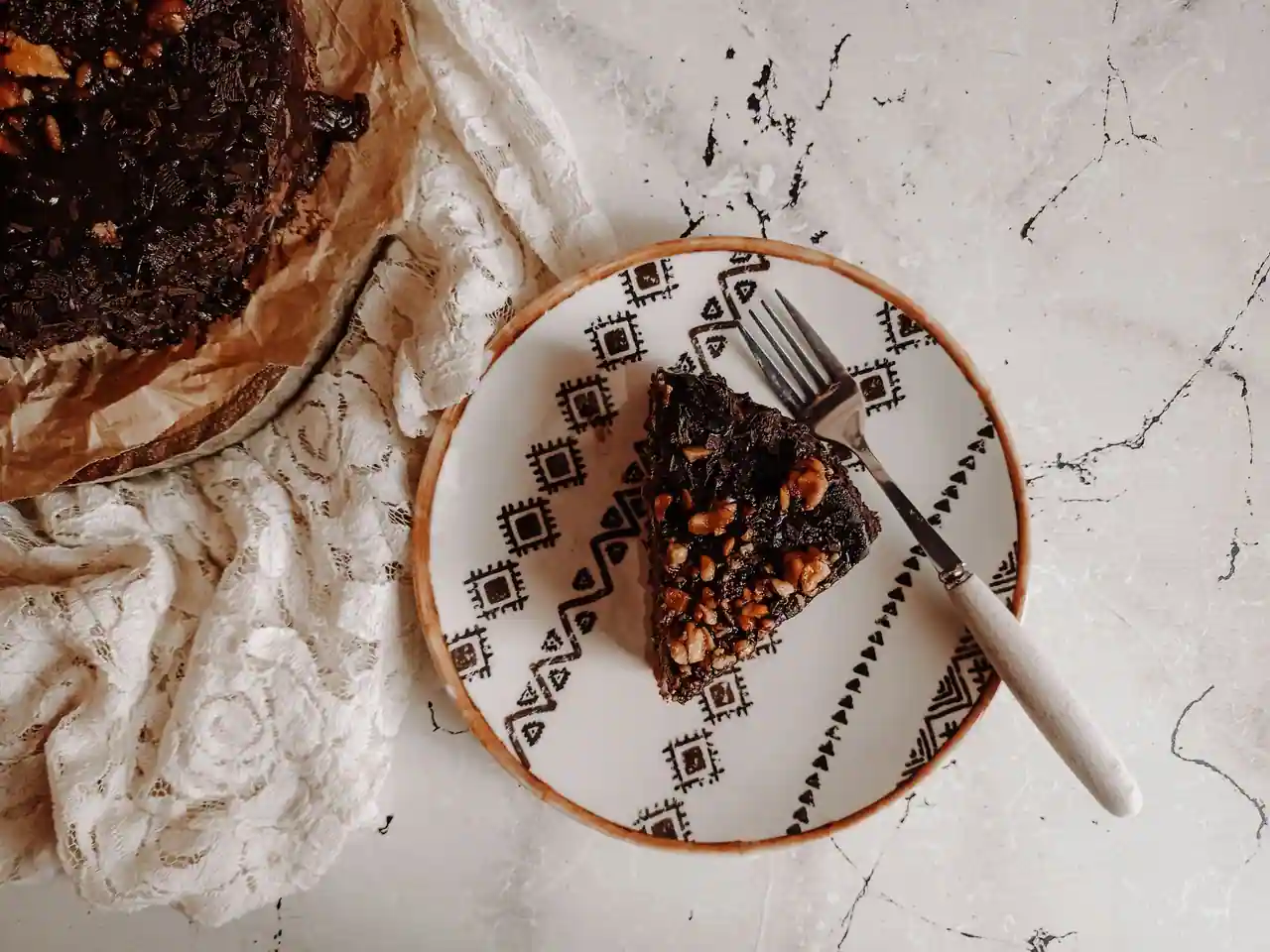 Part de gâteau au chocolat dense parsemée de noix, posée sur une assiette à motifs, vue de dessus