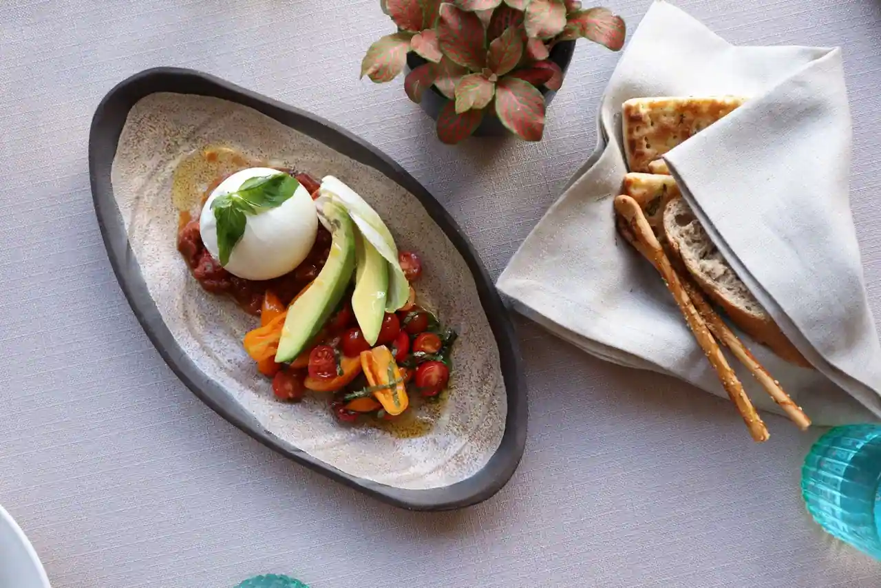 Plat à partager de burrata, tomates cerises, avocat et basilic, servi avec du pain grillé