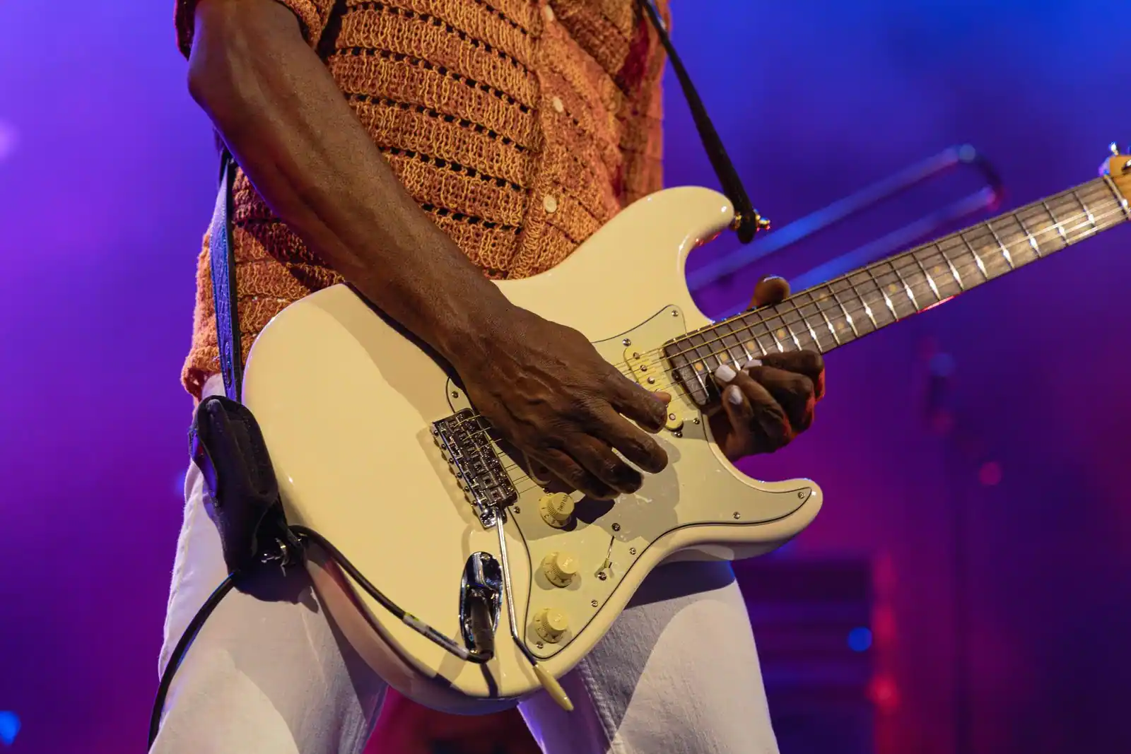 Gros plan sur les mains d'un musicien jouant d'une guitare électrique blanche sur scène