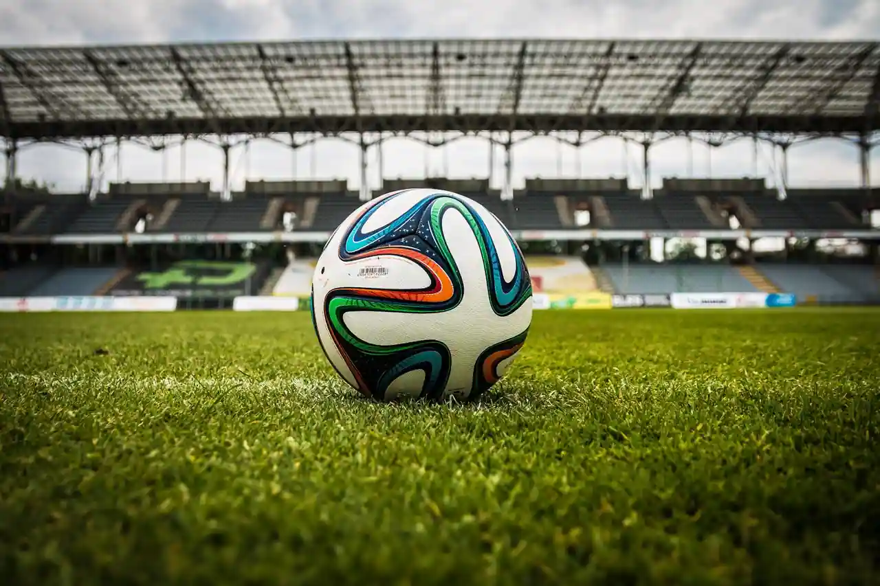 Ballon de football posé sur la ligne blanche d'une pelouse de stade, devant des tribunes vides.