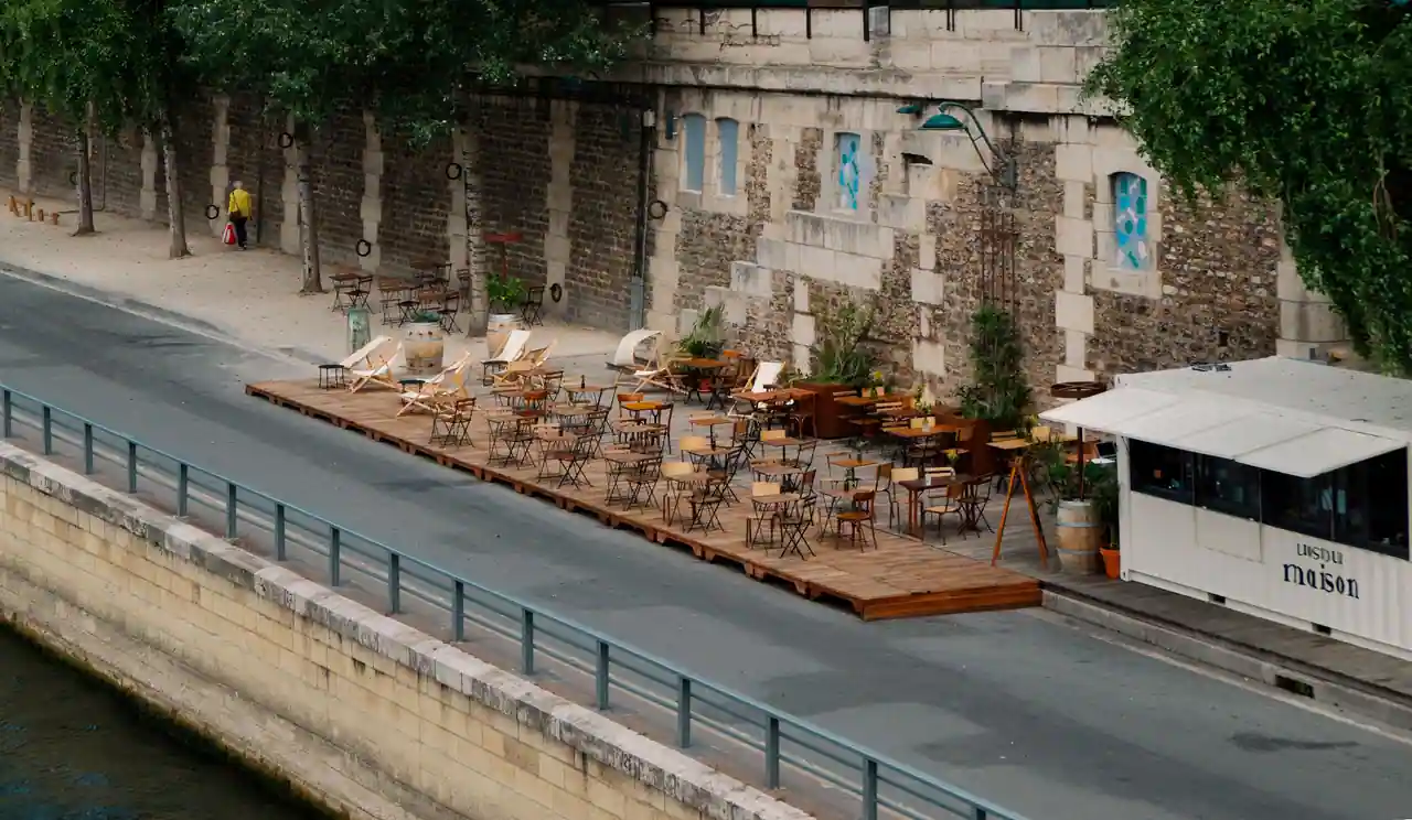 Terrasse de café aménagée sur un quai de Seine, tables et chaises en bois au bord de l'eau