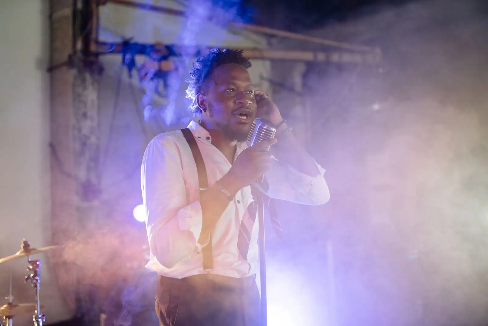 Chanteur sur scène devant un micro vintage, dans une lumière de concert enfumée et colorée.