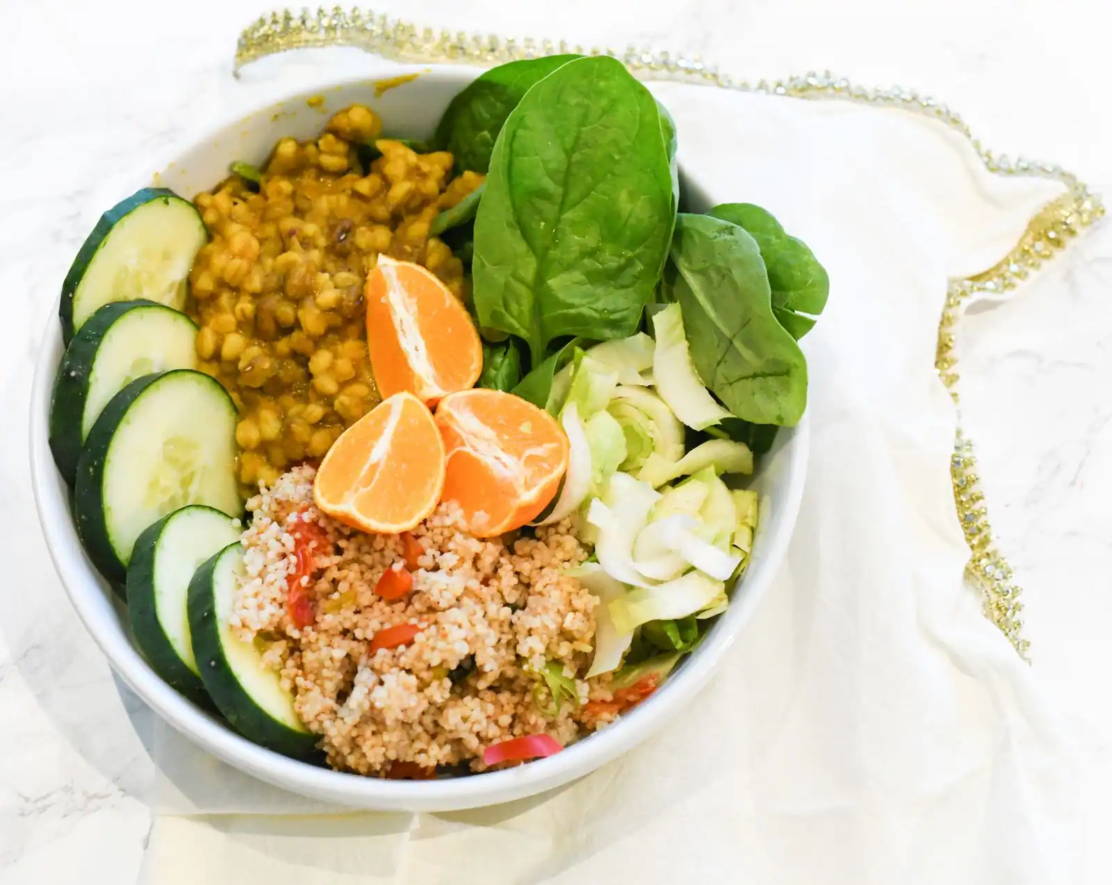 Bol végétarien coloré mêlant légumineuses, quinoa, concombre, épinards et quartiers de clémentine.