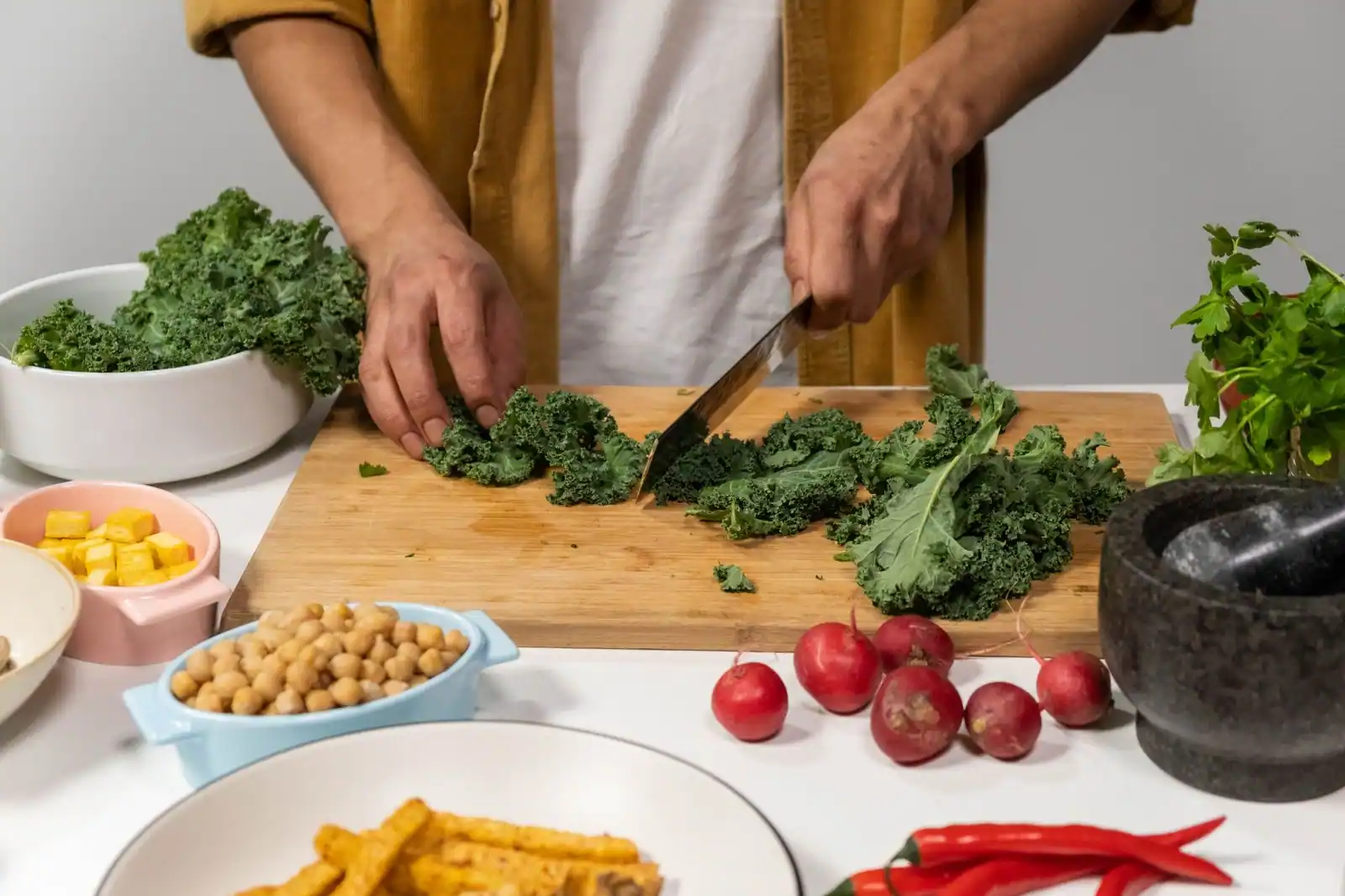 Découpe de chou kale sur une planche, entourée de bols de pois chiches, de tofu et de radis