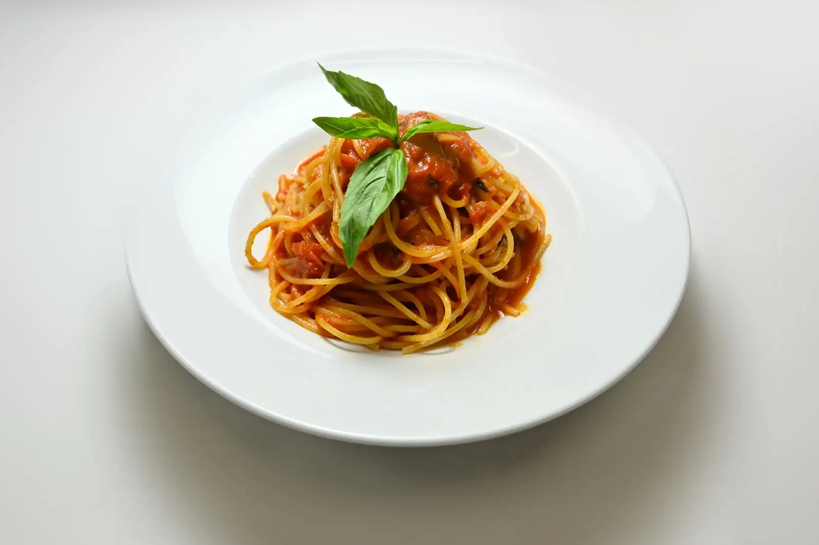 Assiette de spaghettis à la sauce tomate garnis de feuilles de basilic frais.