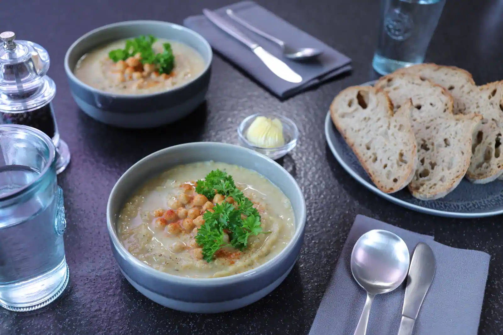 Deux bols de velouté crémeux garnis de pois chiches et de persil, dressés sur une table avec du pain.
